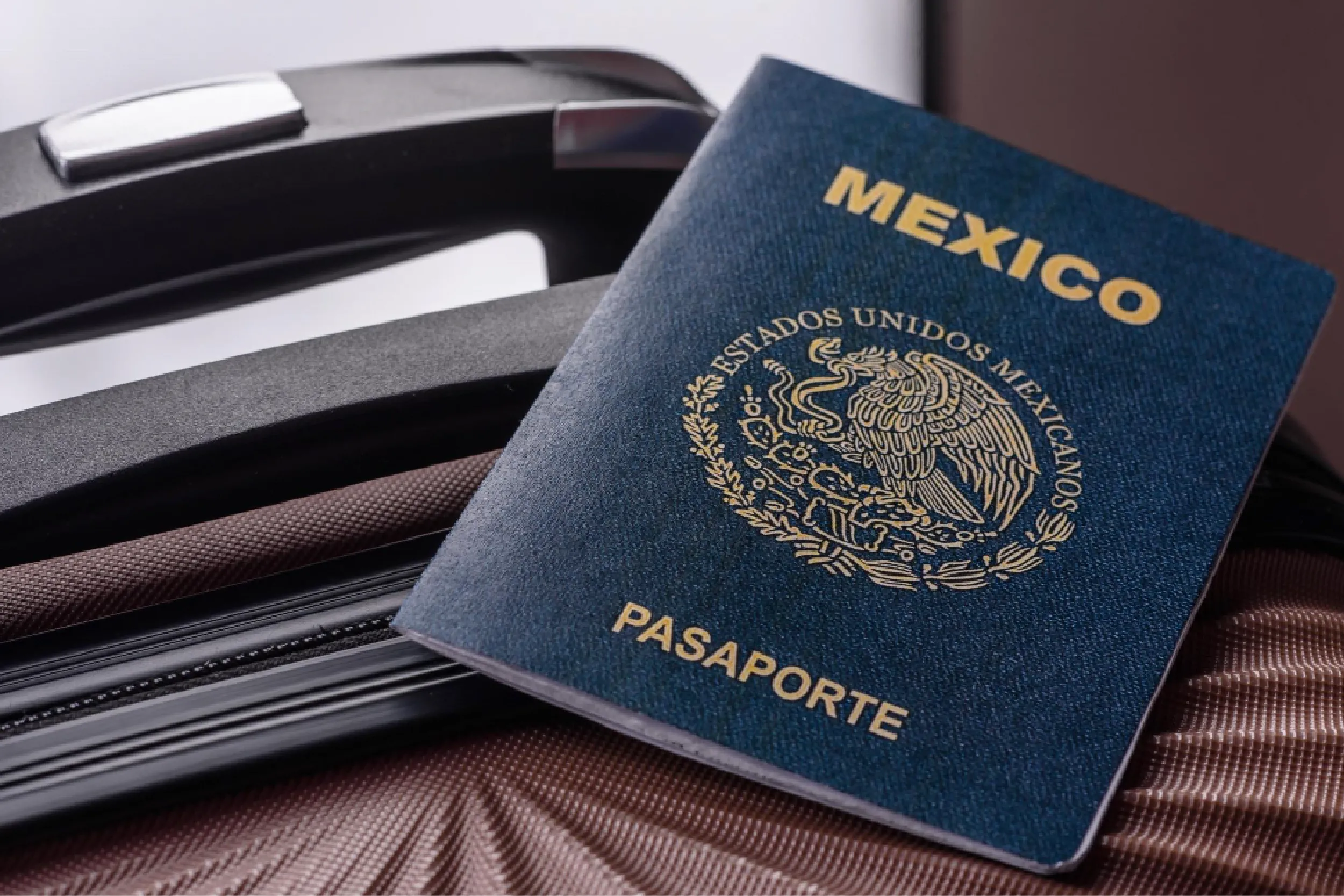 Blue Mexican passport with gold emblem and 'MEXICO' text resting on a dark striped bag.