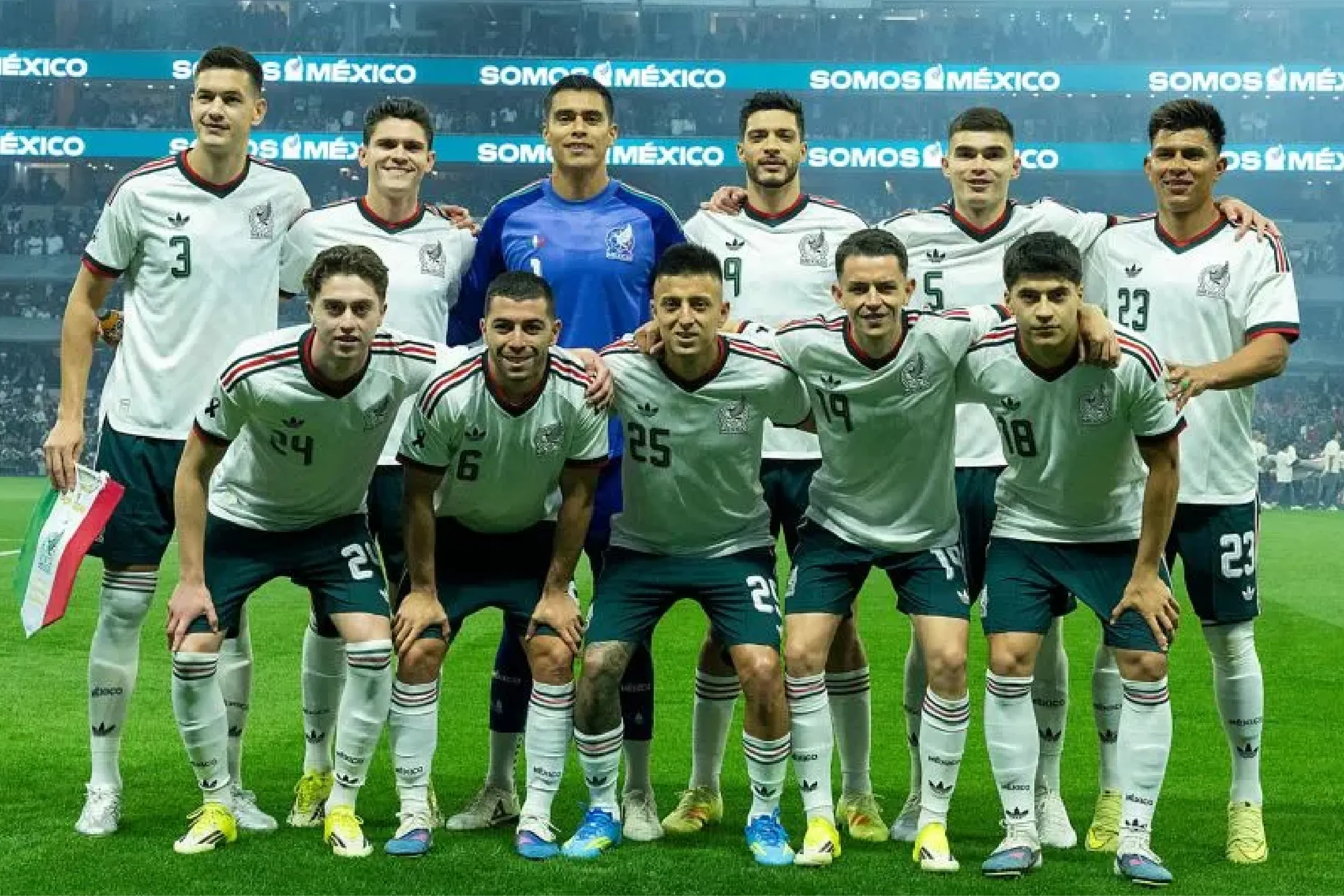 Mexico national football team posing for a group photo on the field, with players in white jerseys and a blue-clad goalkeeper in the center.