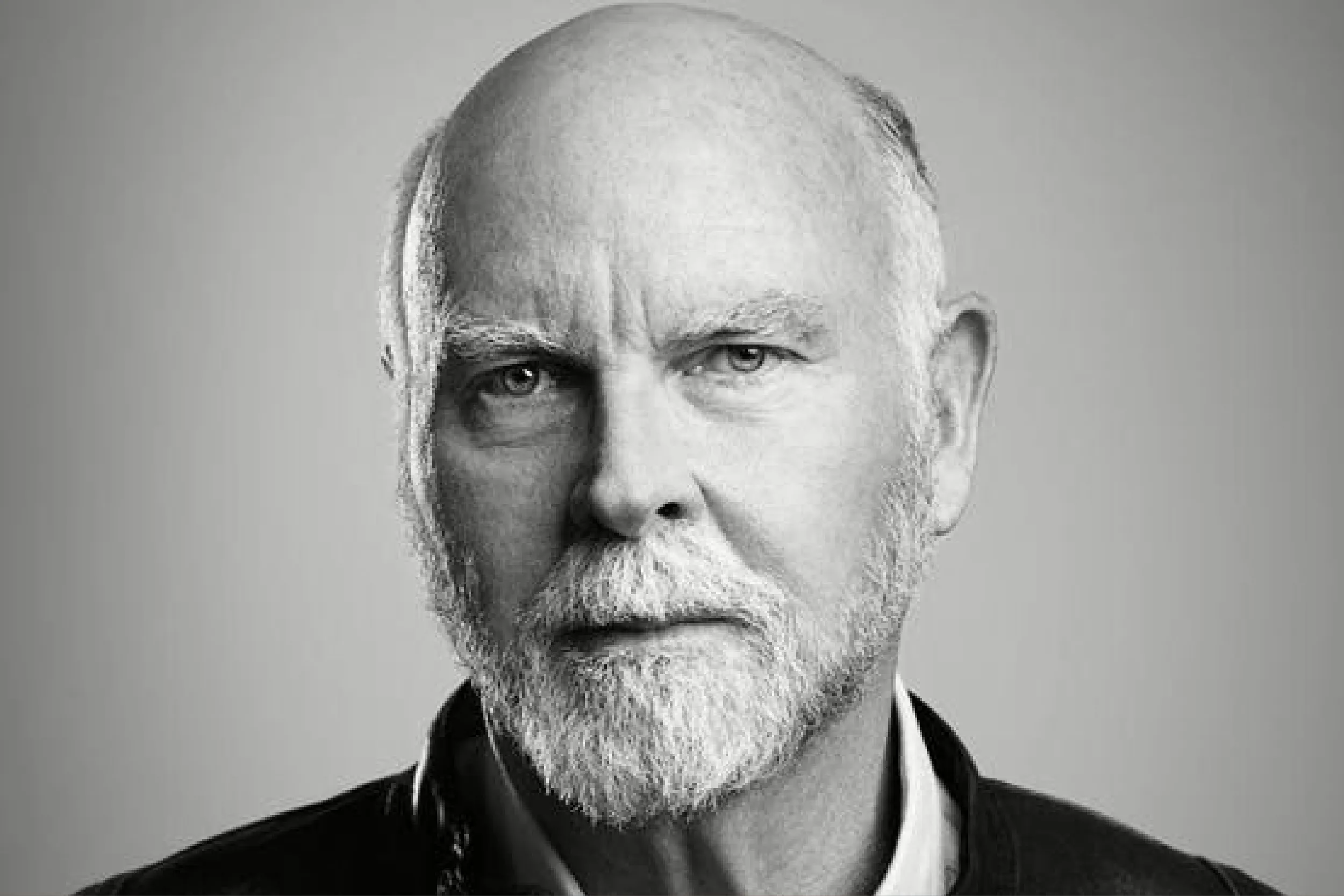 Close-up black-and-white portrait of an older man with a light beard and mustache, wearing a dark jacket.