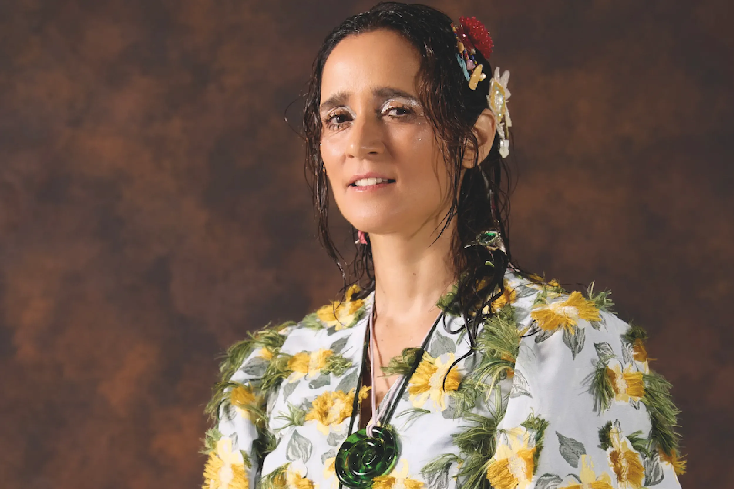 Portrait of a woman in a white floral shirt with yellow flowers and green leaves, facing the camera.
