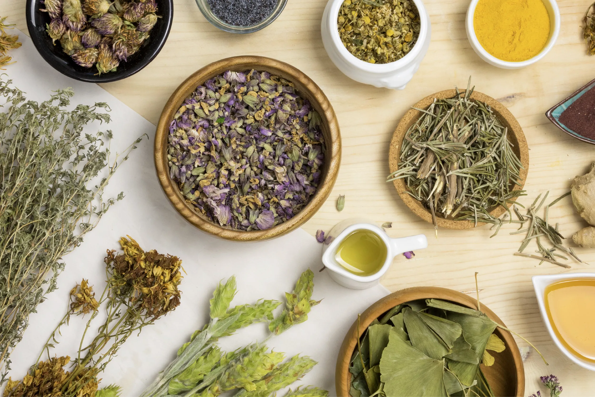 Top-down view of assorted dried herbs and spices in bowls and on a wooden table.