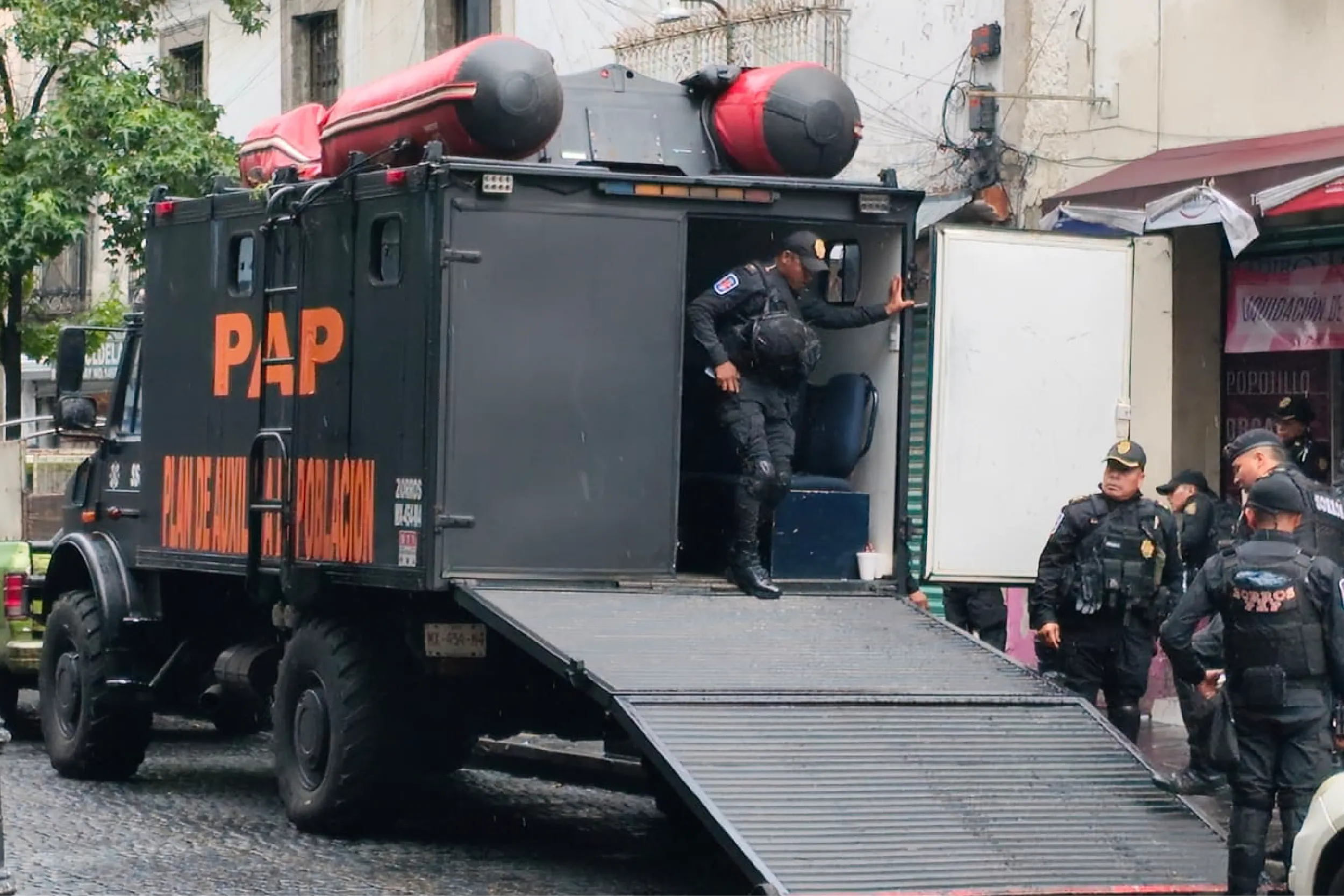 Armored police vehicle with a lowered ramp and officers standing nearby on a city street.