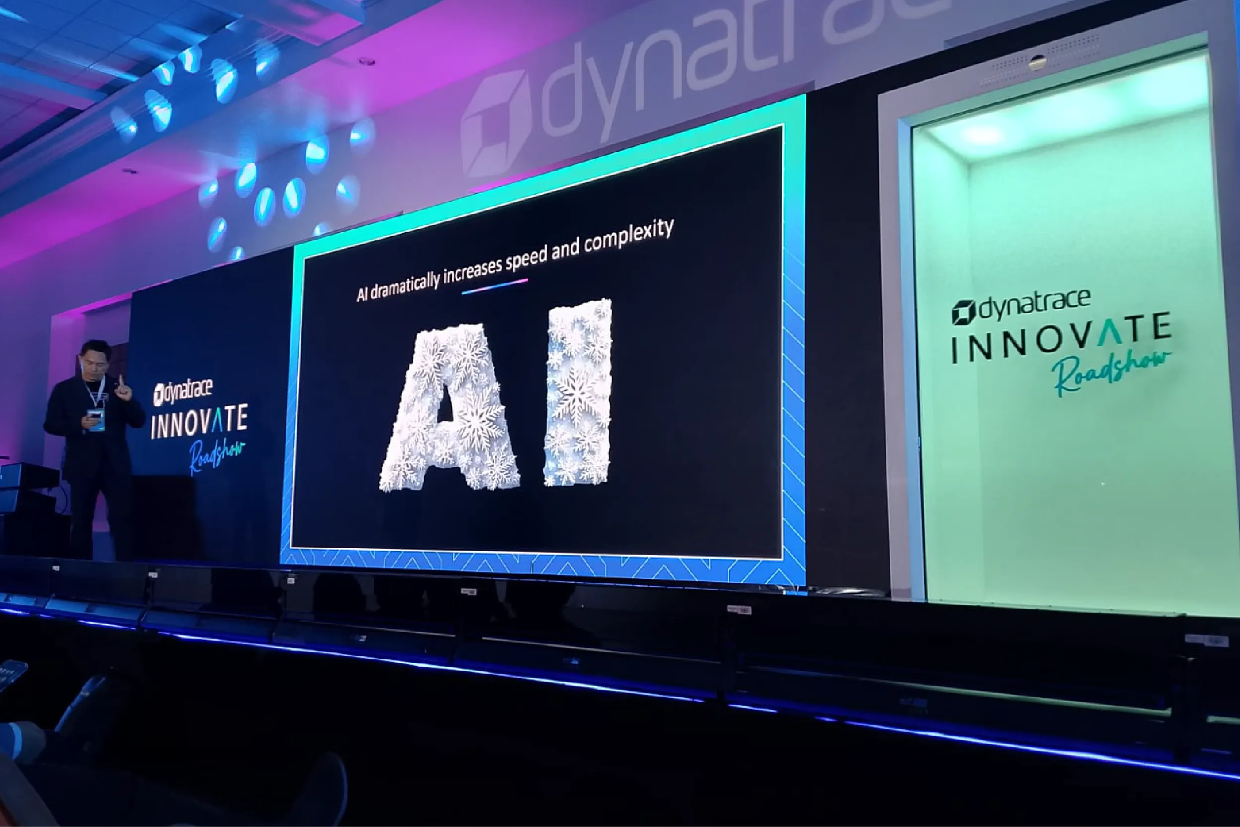 Presenter on a stage at a Dynatrace Innovate Roadshow with a slide reading 'AI dramatically increases speed and complexity'