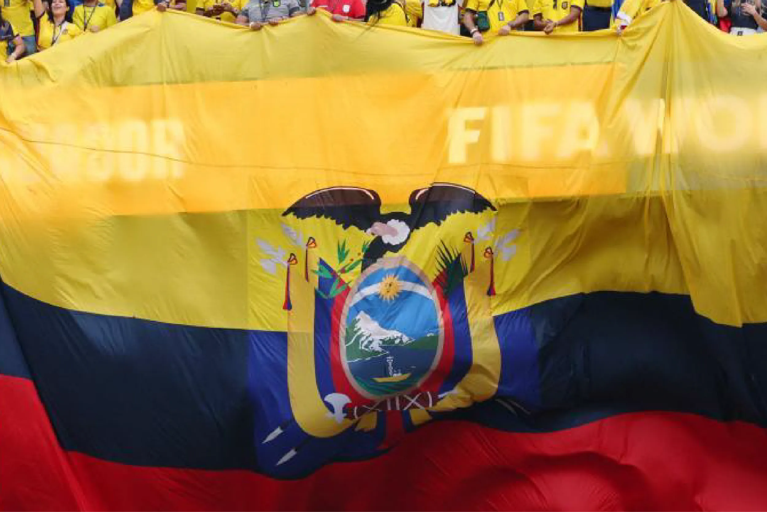 Crowd behind a large yellow banner with a central coat-of-arms emblem, flanked by blue and red fabric.