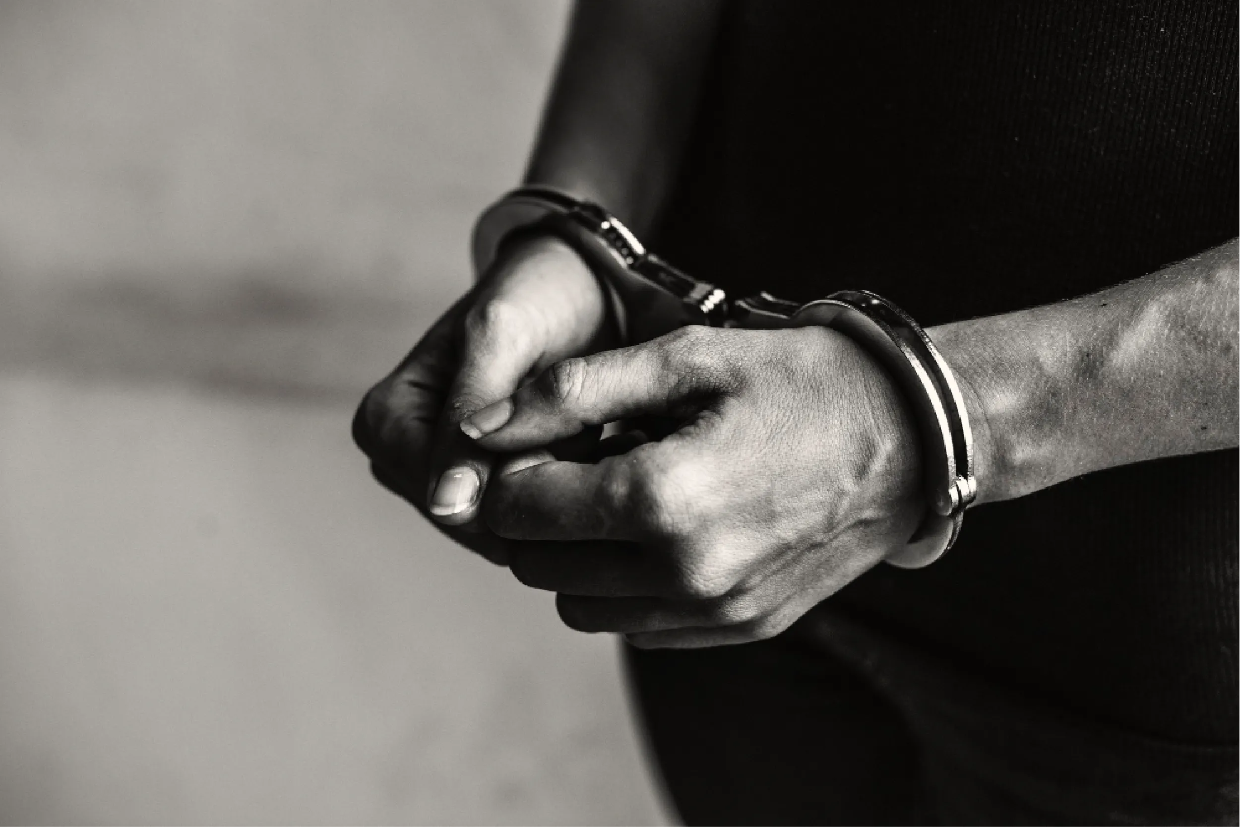 Close-up of a person's hands bound with metal cuffs and leather straps in a black-and-white photo.