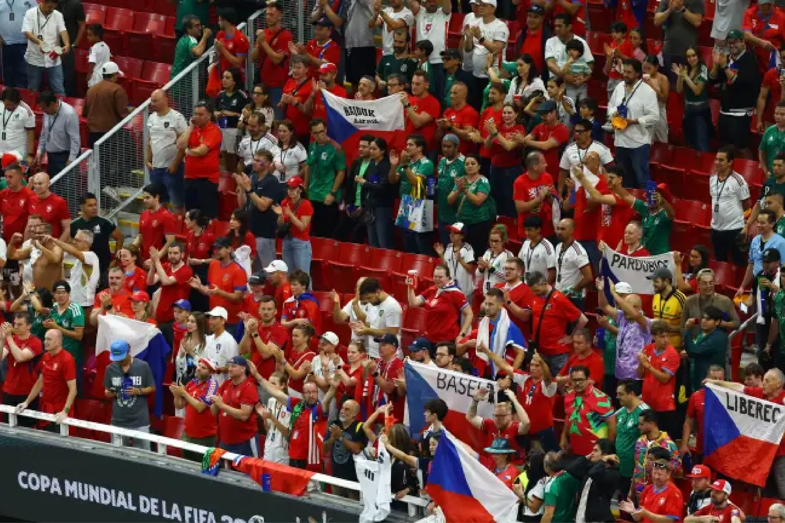 Large crowd of sports fans in red, green, and white cheering from stadium stands, many waving flags and banners.