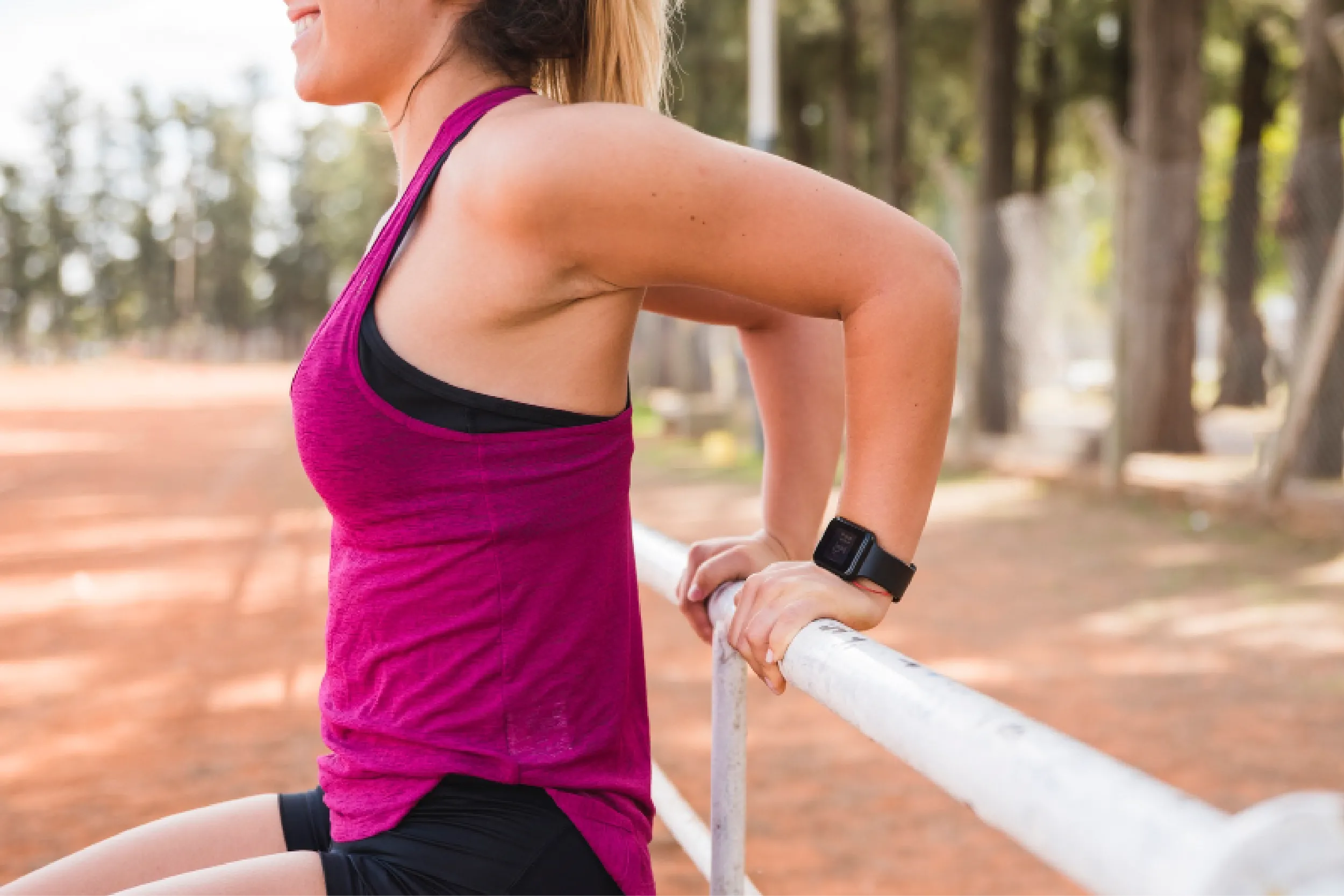 Woman wearing a pink athletic top rests her arms on a railing outdoors, likely after running in a park or track.