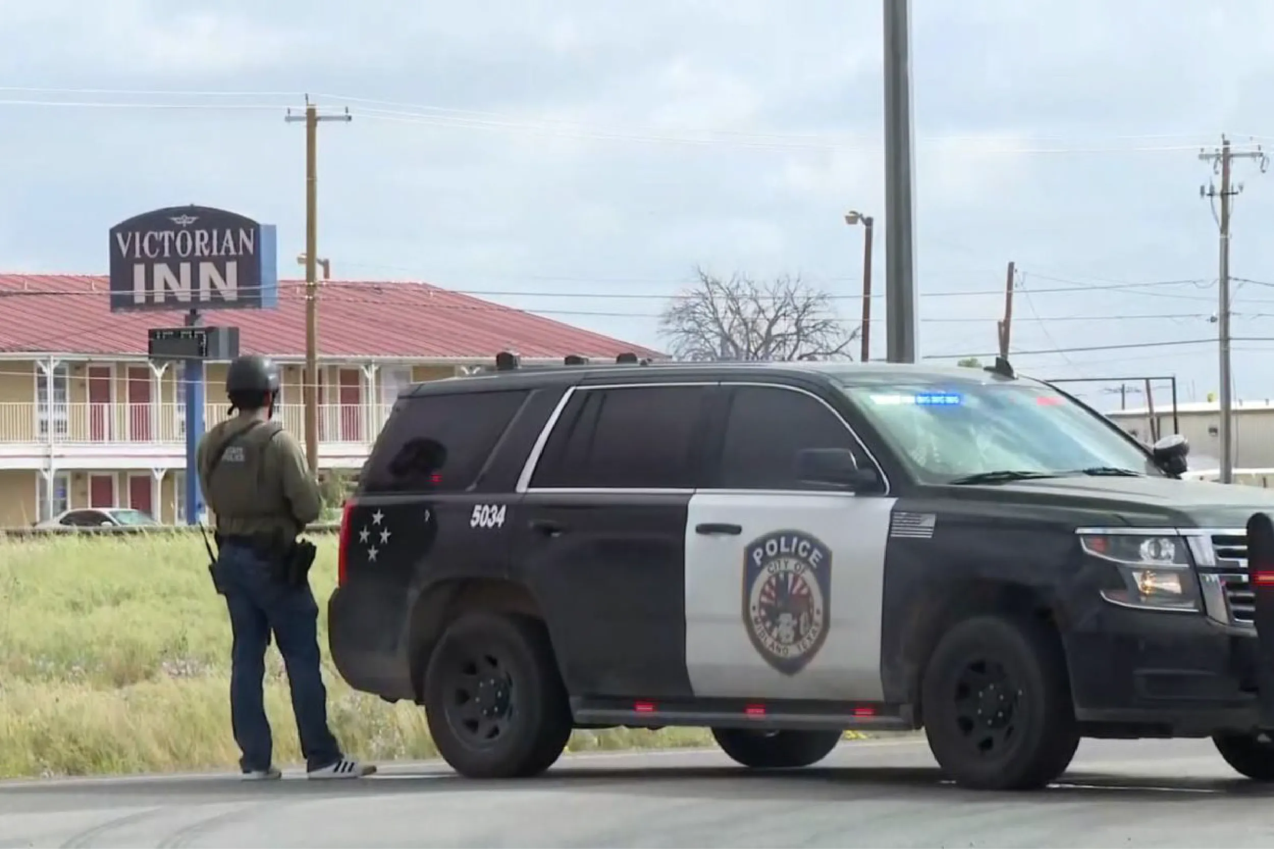 Police SUV parked on the street with a uniformed officer standing nearby, in front of a motel sign that reads 'Victorian Inn'.