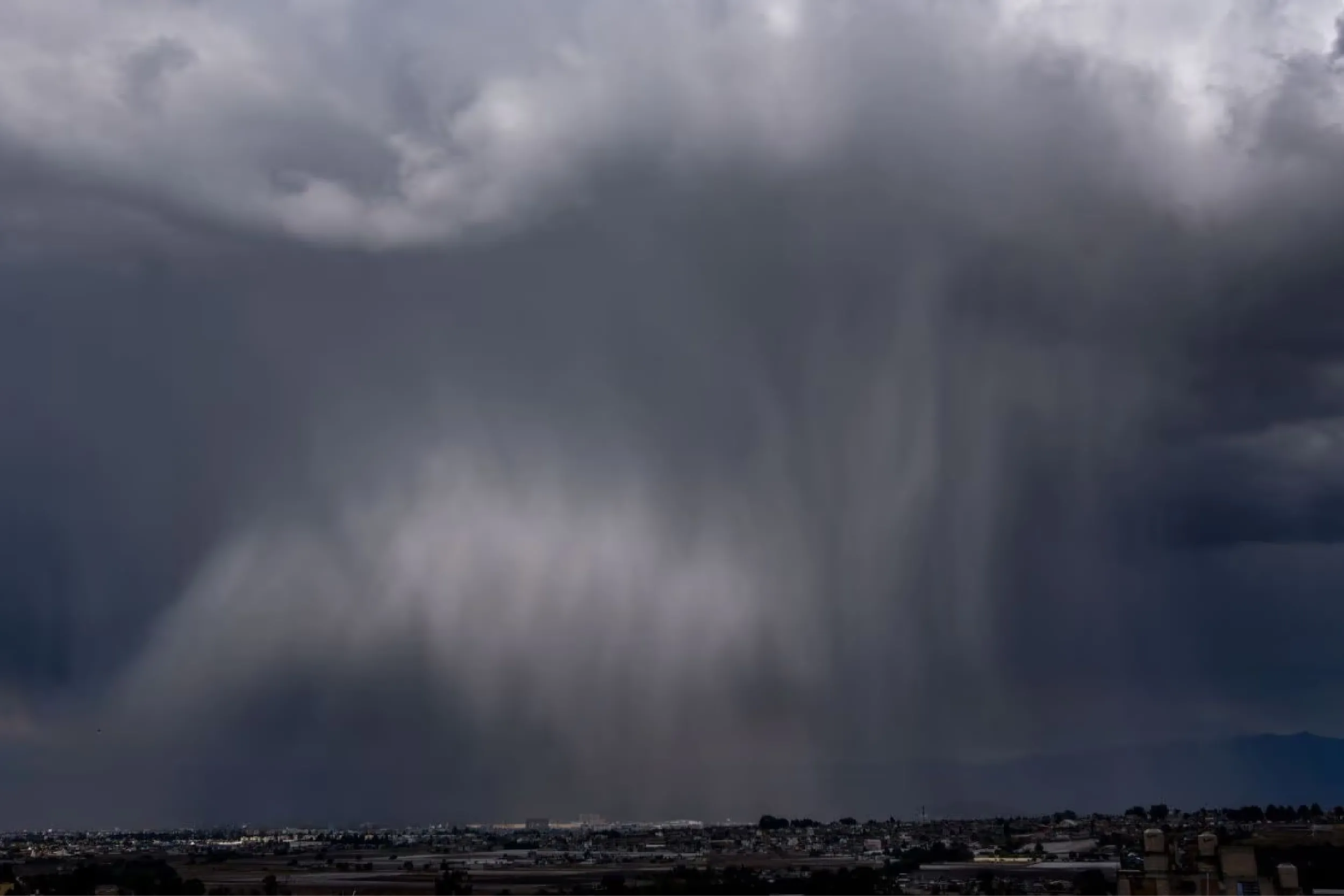 Dark storm clouds looming over a flat landscape with a distant town on the horizon, conveying ominous weather.