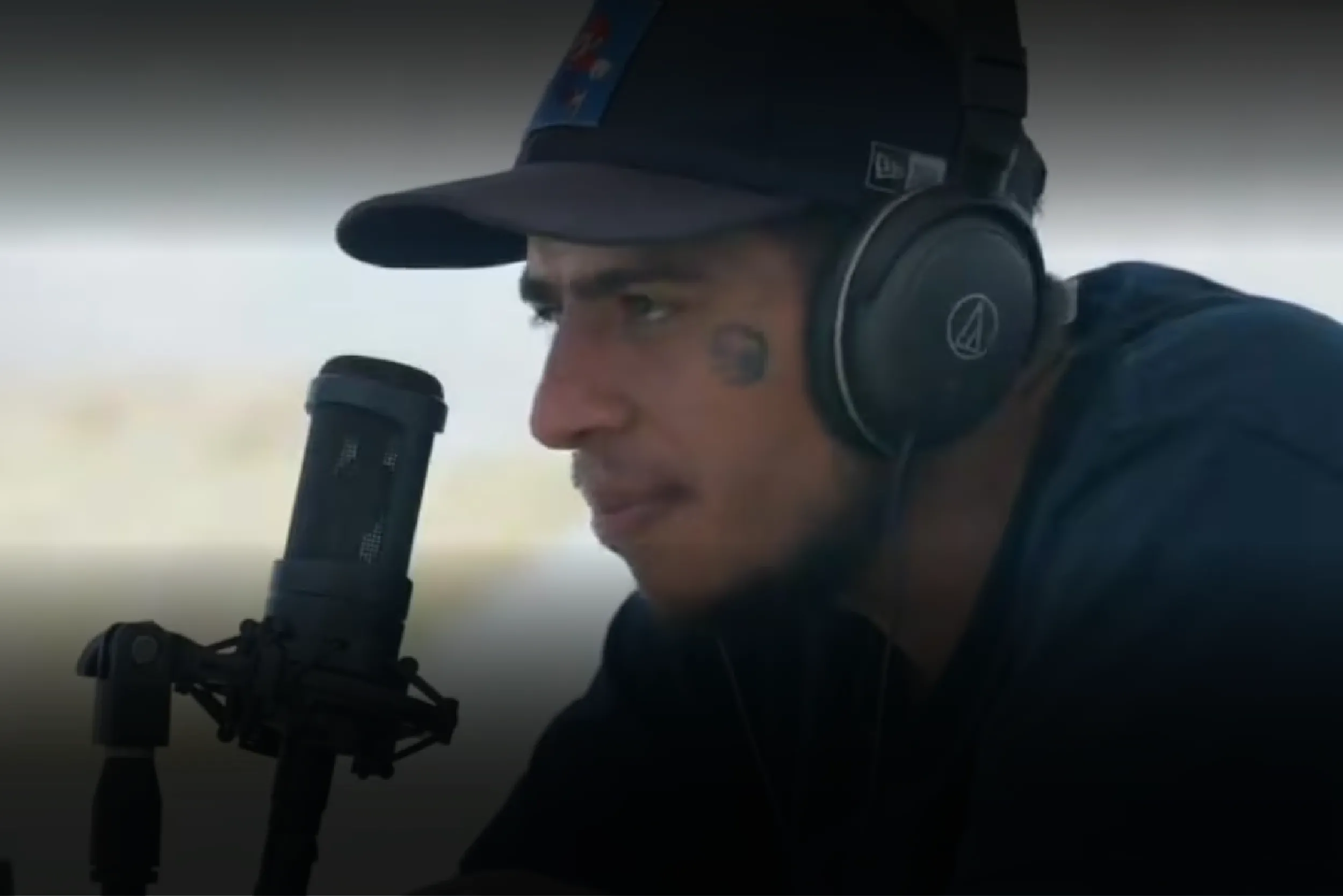 Close-up of a man wearing a cap and over-ear headphones speaking into a professional microphone