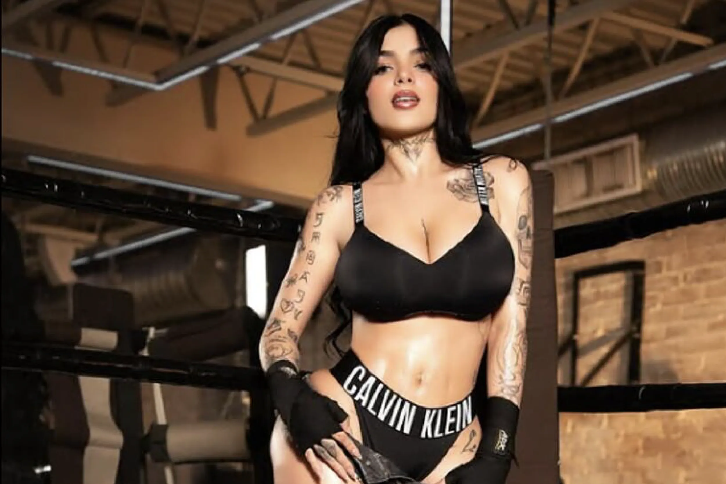 Tattooed woman in black underwear poses in a gym setting, wearing a Calvin Klein waistband.