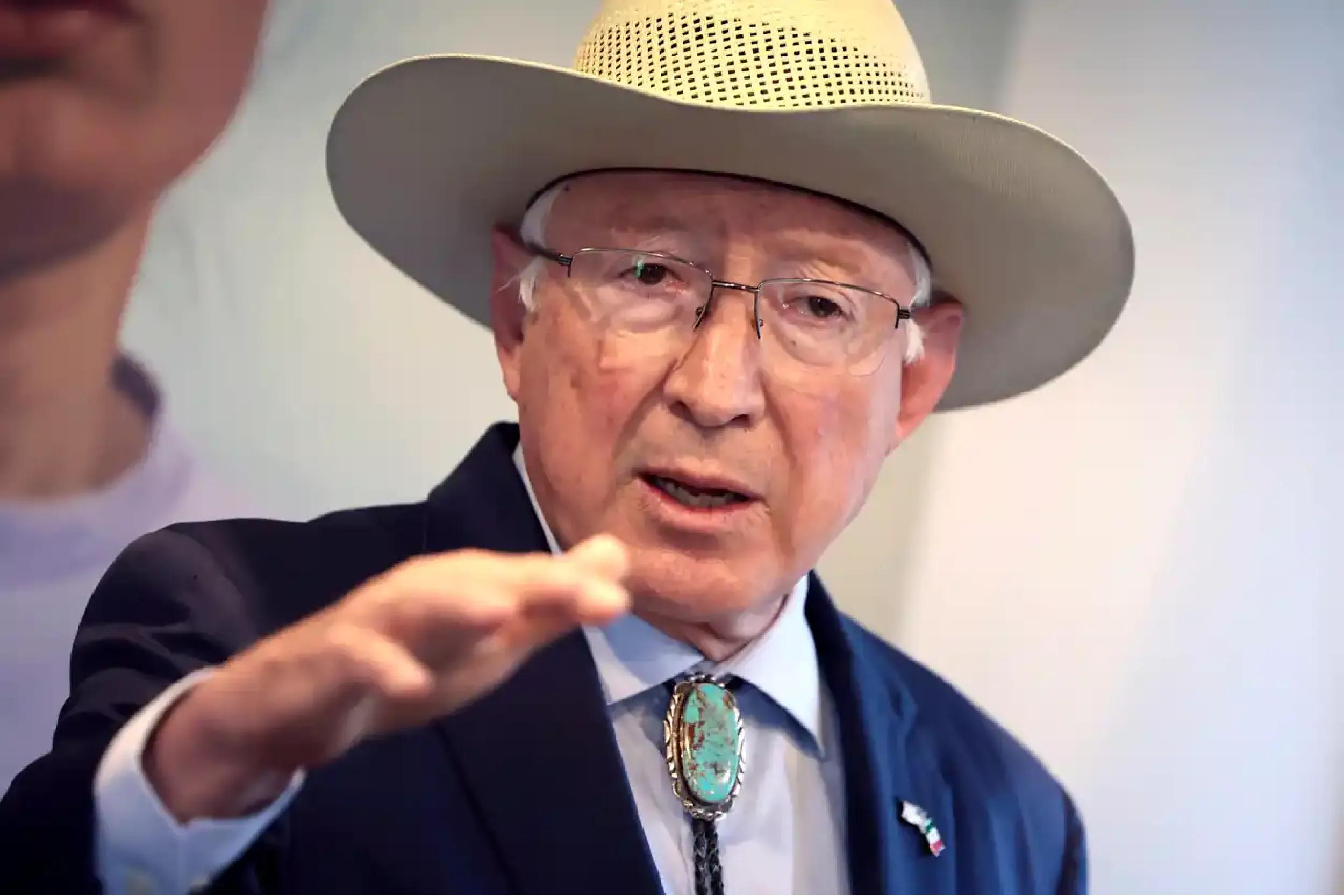Elderly man in a wide-brim hat and glasses gestures toward the camera during a discussion panel.