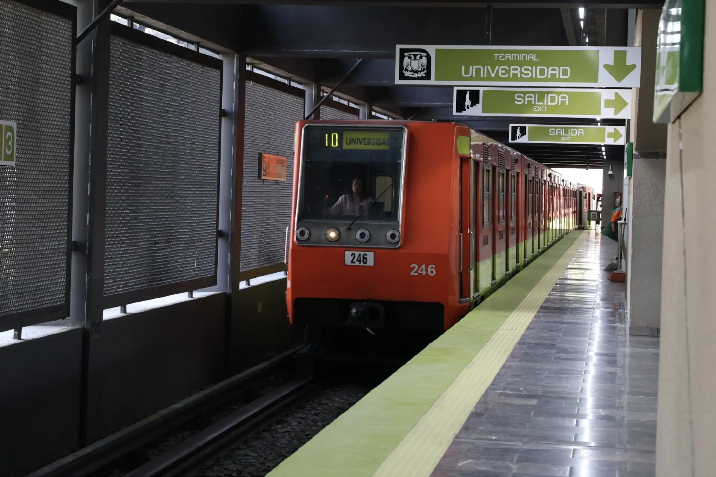 Orange metro train at a station platform with green signs reading Universidad and Exit (Salida).