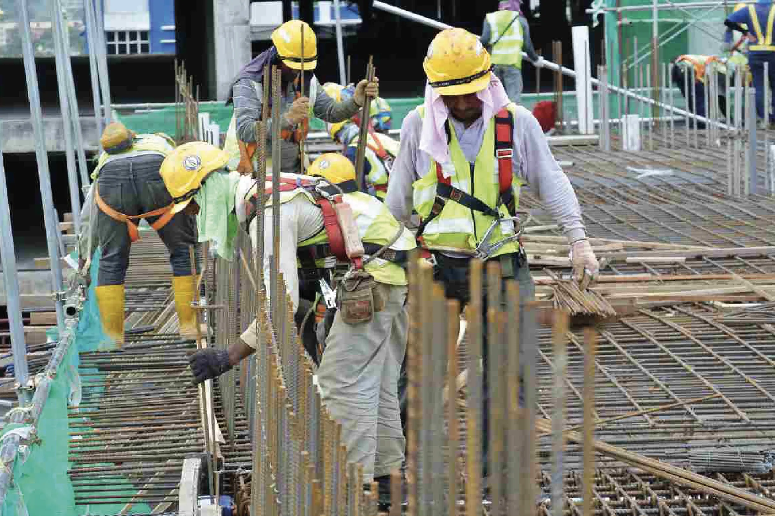 Construction workers in yellow helmets and high-visibility vests working on a rebar framework at a building site.