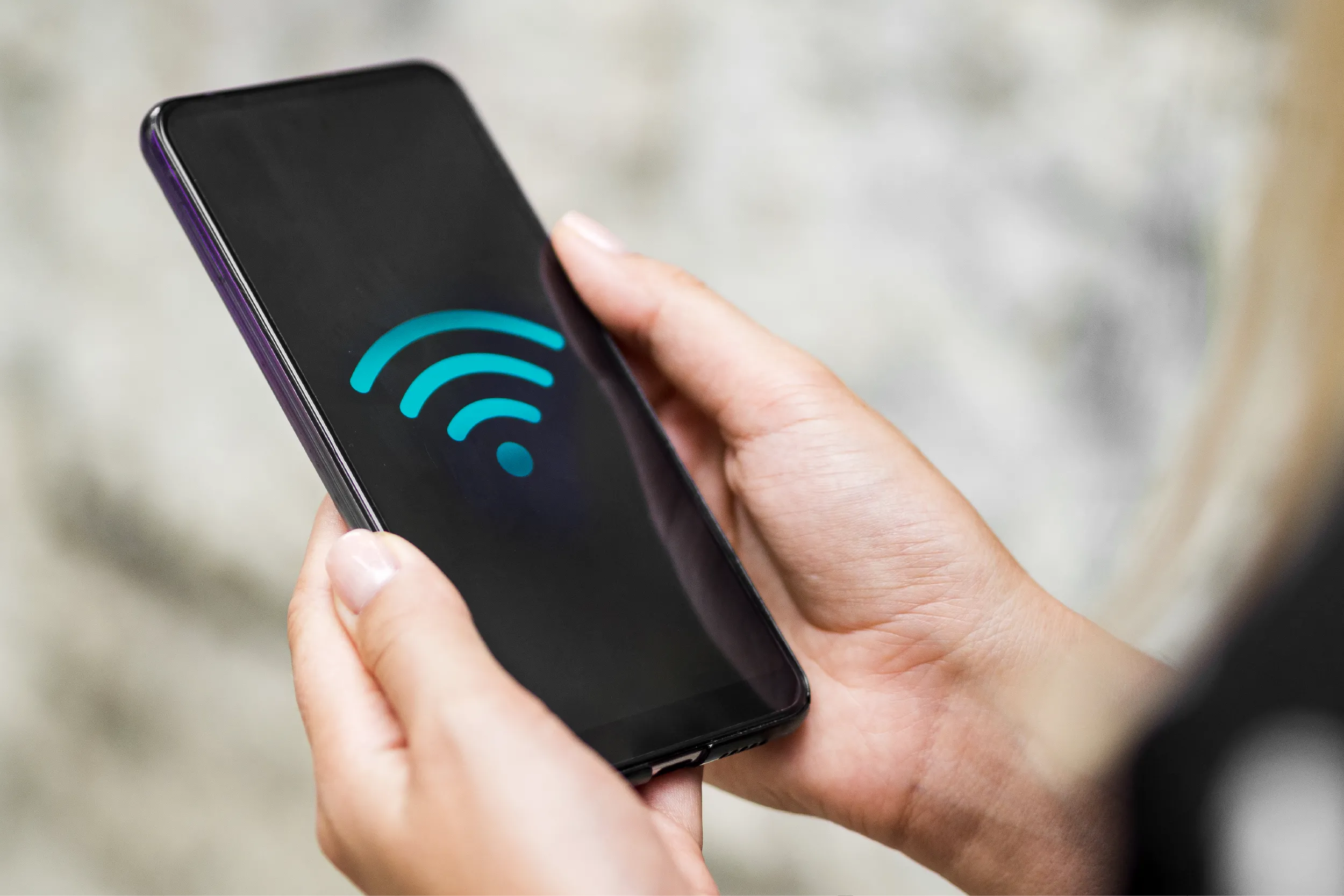 Hand holding a smartphone displaying a blue contactless payment icon on the screen, indicating NFC payment.