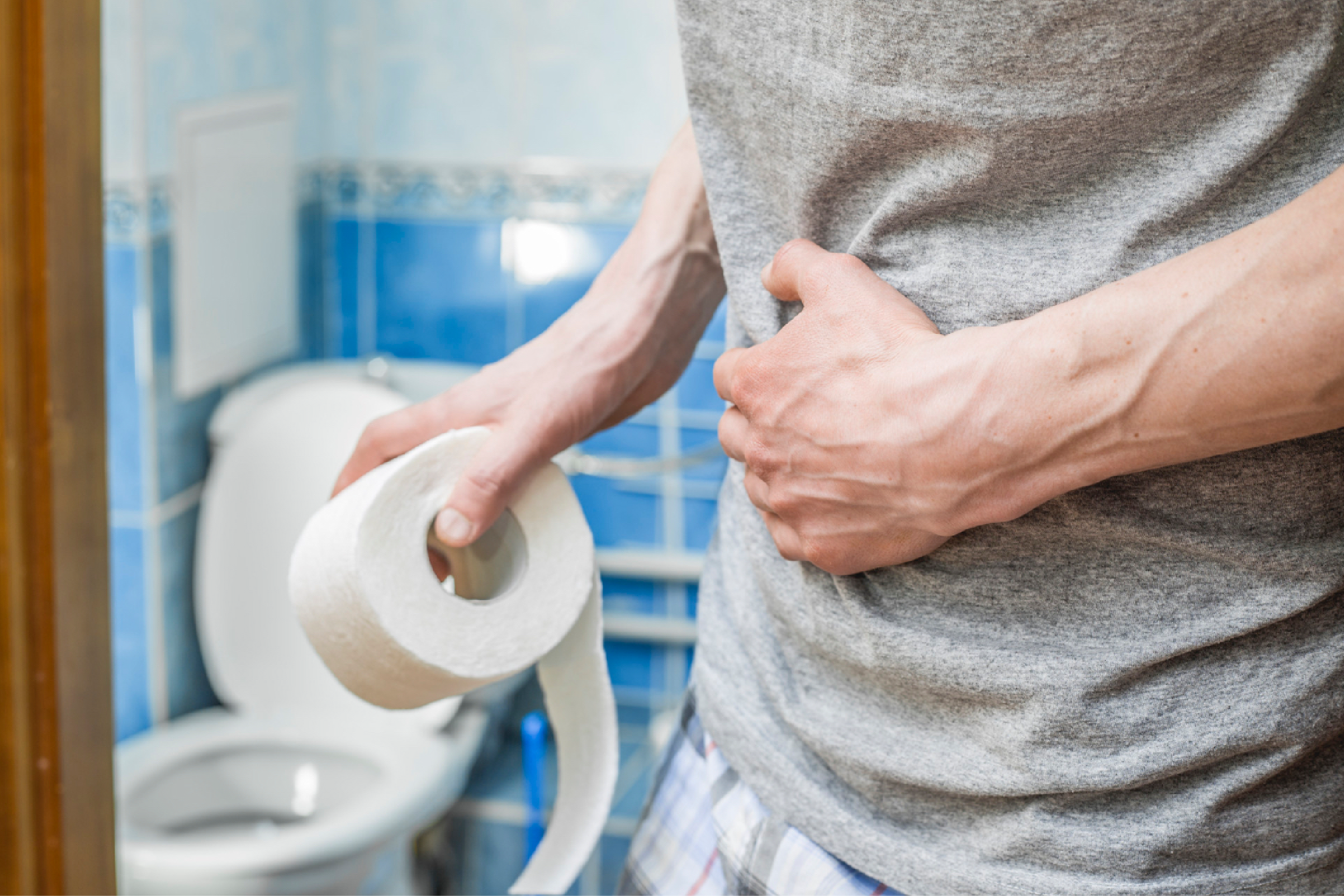 Person holding a roll of toilet paper in a bathroom, with a toilet visible in the background.