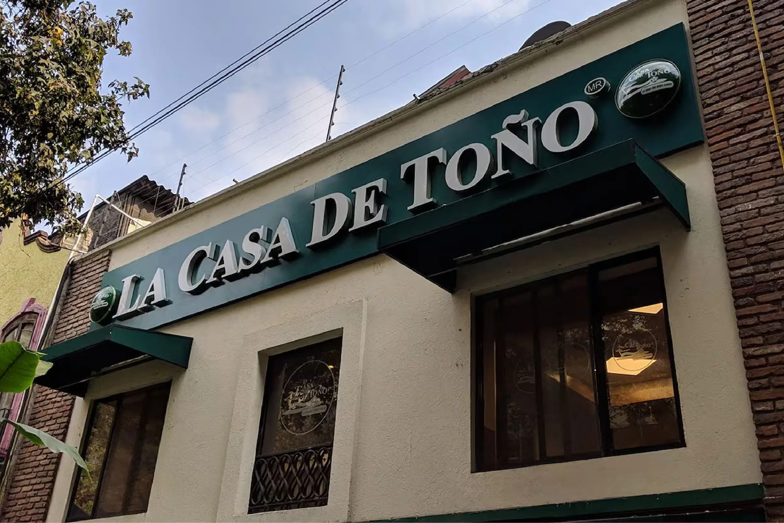 Storefront sign reading 'LA CASA DE TOÑO' on a teal/green awning above a doorway.