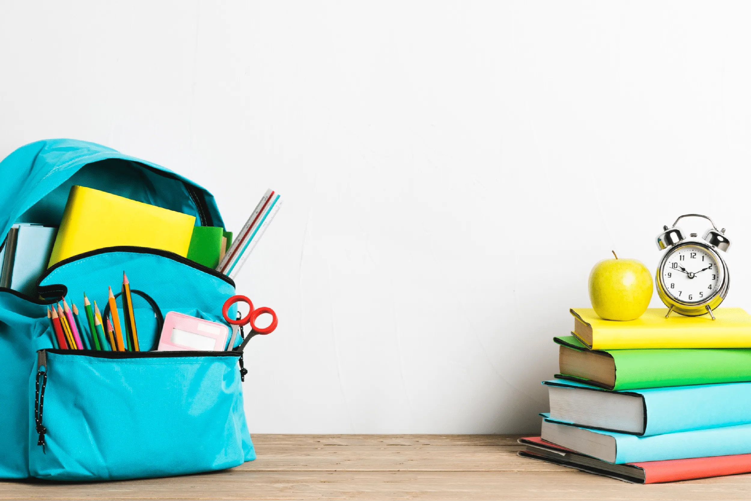 Open turquoise backpack overflowing with school supplies—pencils, notebooks, and scissors—on a wooden desk beside a stack of colorful books and a clock.